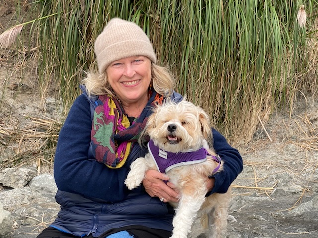 Pam Bell outdoors in Fort Bragg holding her dog and smiling.